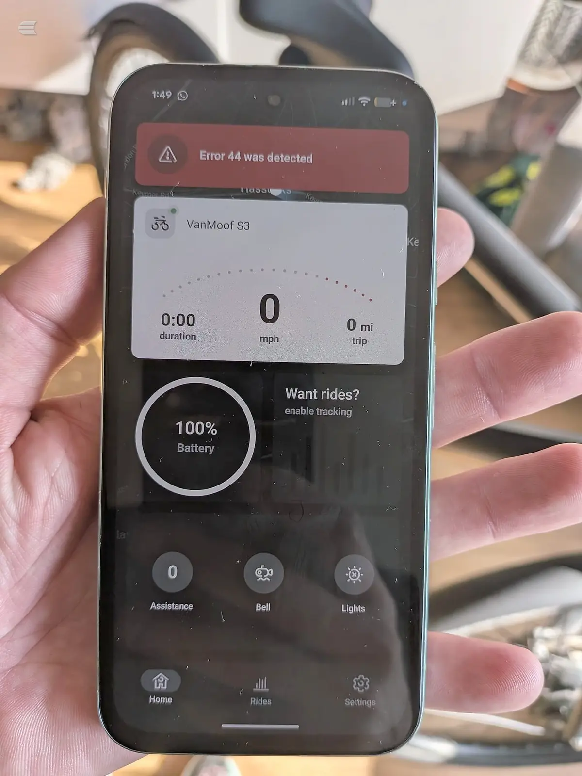 Smartphone screen displaying VanMoof S3 e-bike app interface with error message and battery status, held in hand over wooden surface.