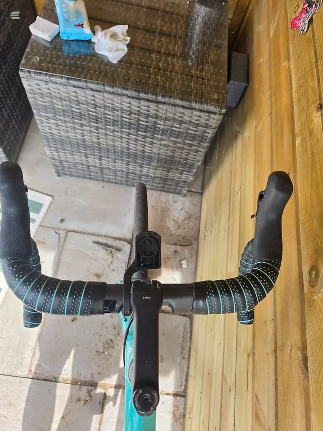 Teal and black drop-bar road bike viewed from above, seated position, on wooden decking next to concrete paving. Drive side visible.