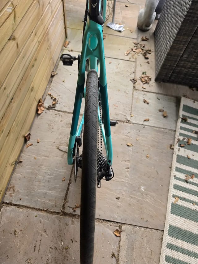 Teal and black gravel or hybrid bike on a paved ground, overhead view, drive side, between wooden fence and green anti-slip mat.