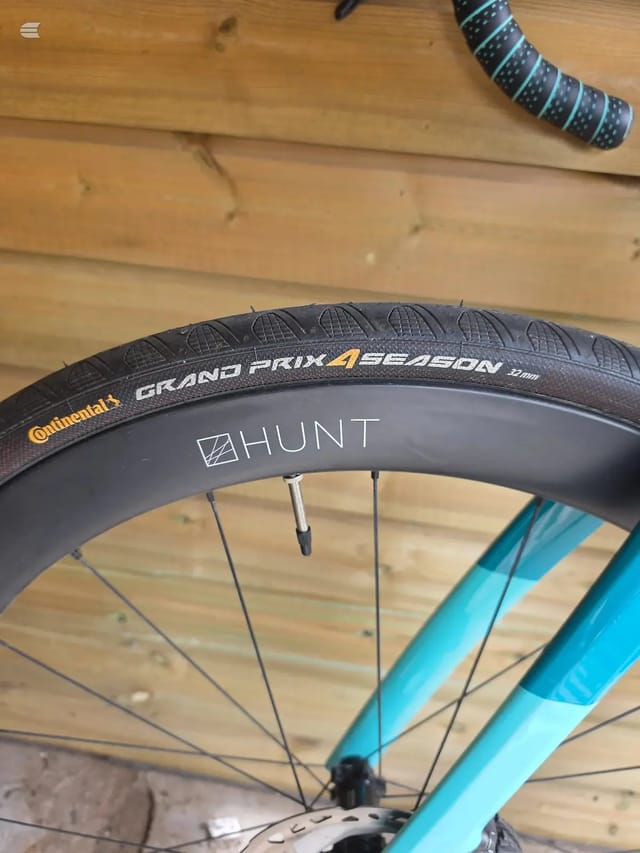 Close-up of a bicycle wheel with Continental Grand Prix 4 Season tyre and Hunt rim, on wooden floor, drive side.