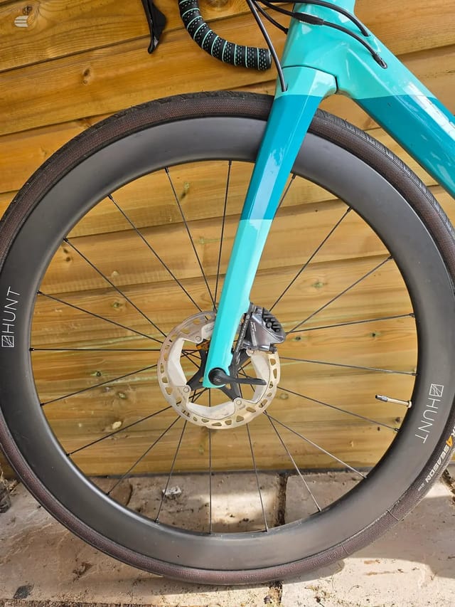 Turquoise gravel bike front wheel with disc brake, Hunt carbon rim, on wooden decking. Drive side view.