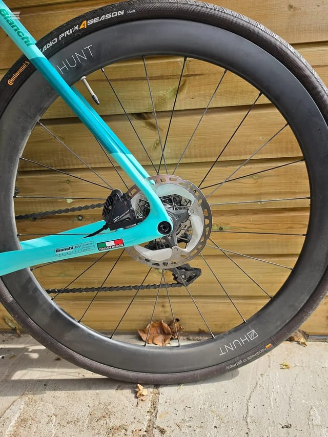 Turquoise Bianchi gravel bike, rear wheel close-up showing disc brake and hub, drive side, on wooden decking.