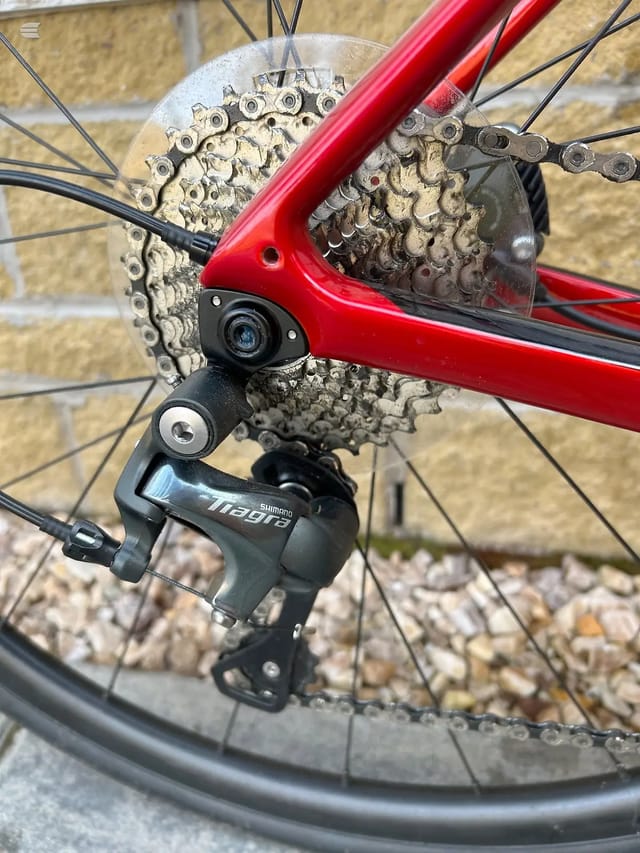 Shimano Tiagra rear derailleur and cassette on red bike frame, drive side close-up against brick wall.
