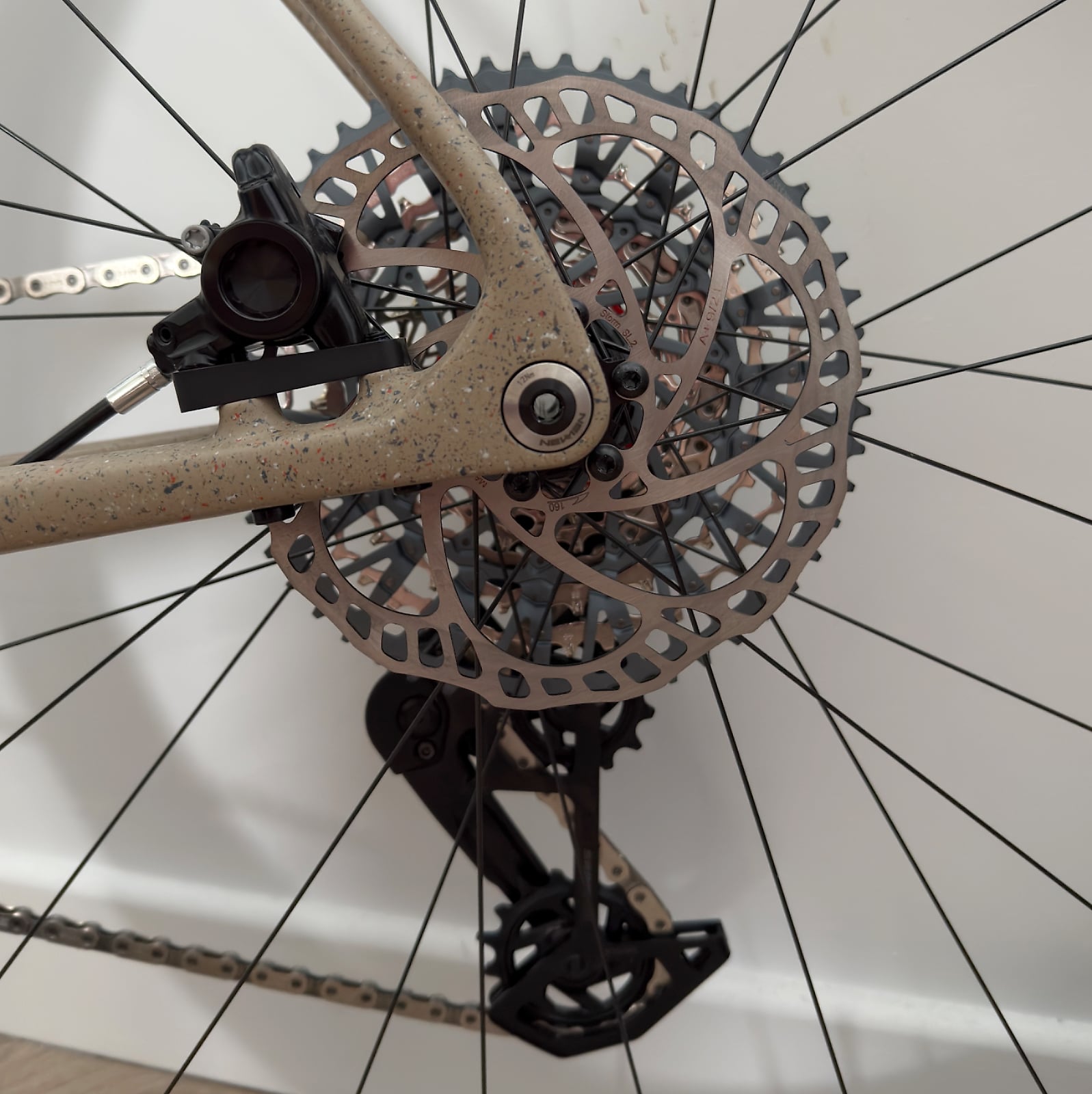 Close-up of disc brake system on gravel bike, showing rotor and caliper detail, drive side, against white background.