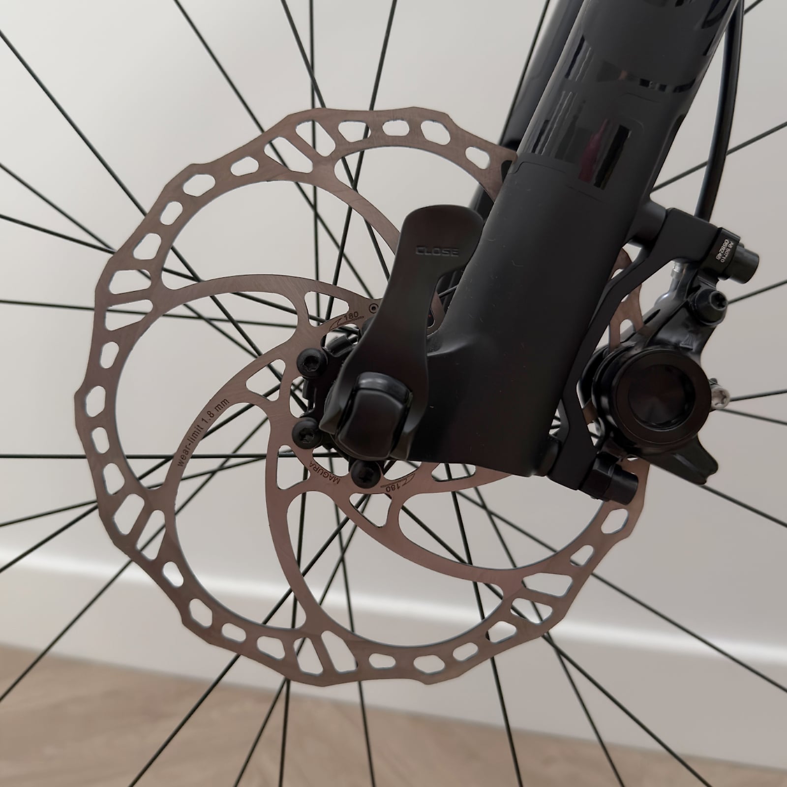 Close-up of disc brake system on black mountain bike, front wheel with brown rotor and hydraulic caliper, drive side angle against white background.