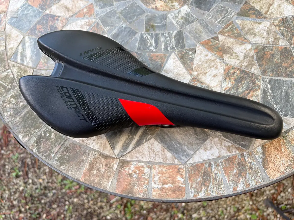 Black bicycle saddle with red accent stripe on textured stone patio, top view.
