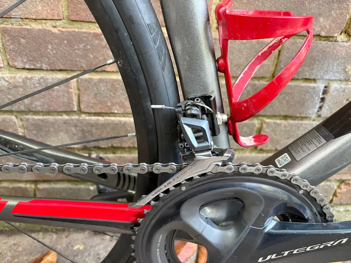 Close-up of Shimano Ultegra crankset and chain on red and black road bike, drive side, against brick wall.