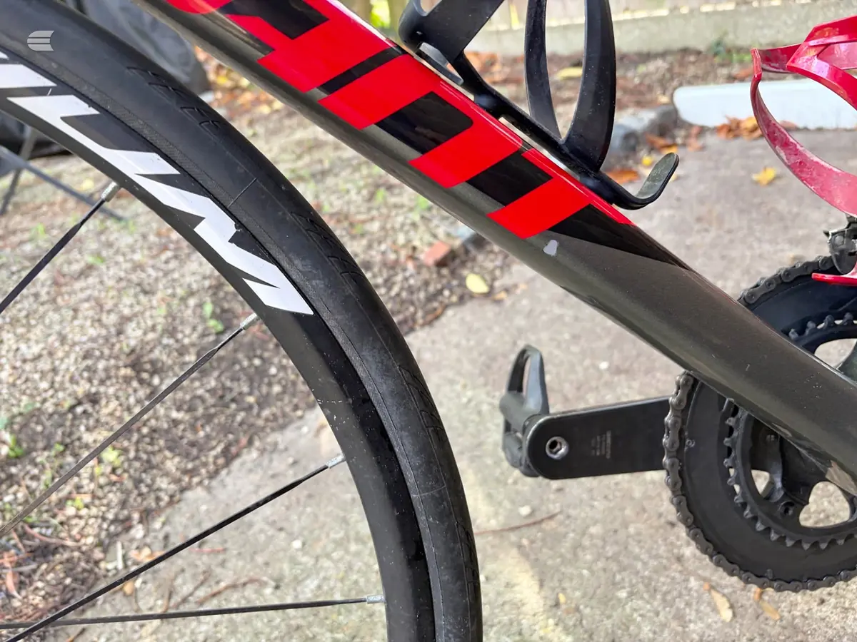 Close-up of red and black road bike frame and components, drive side, outdoors on pavement with gravel background.
