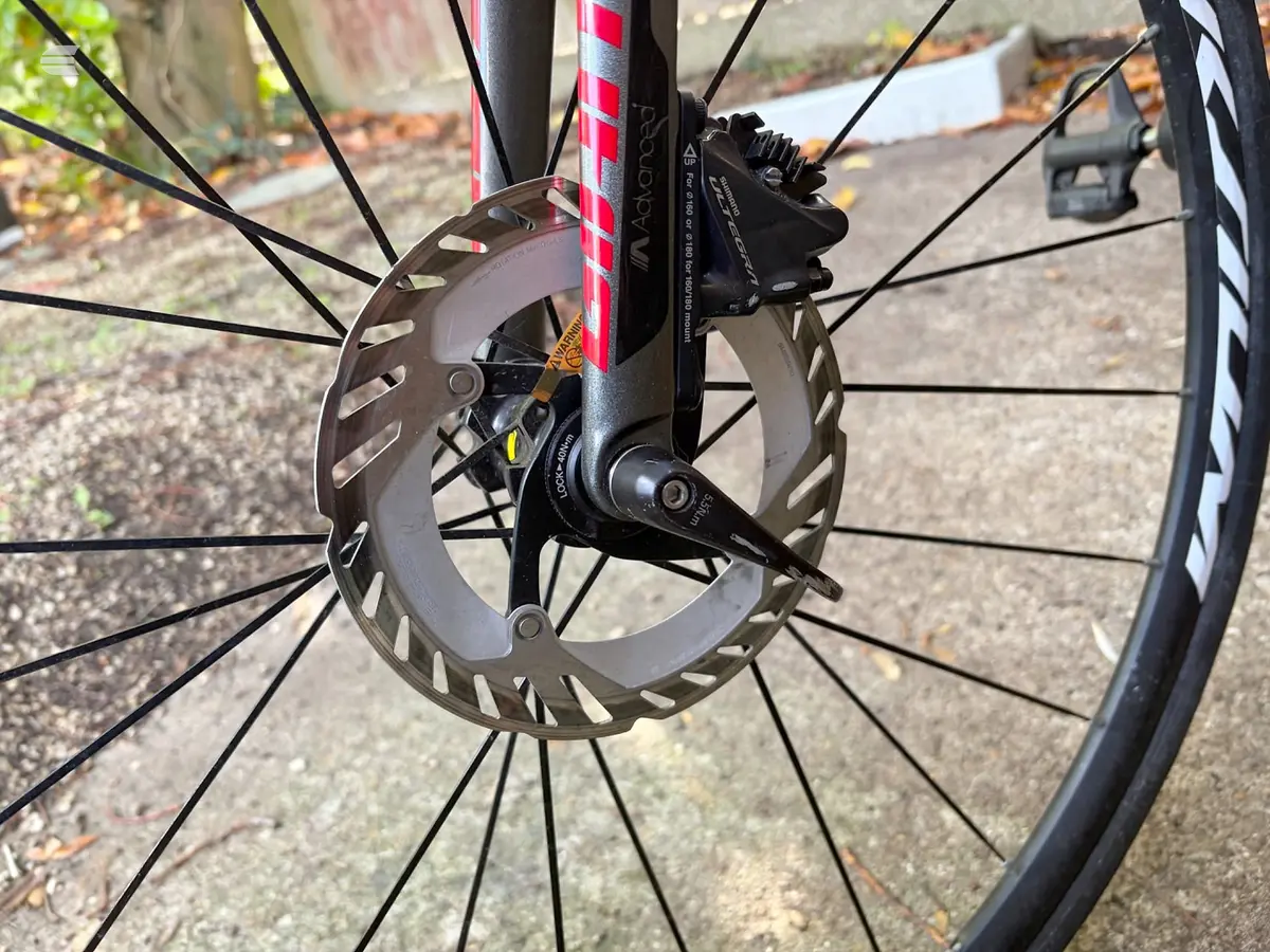 Close-up of hydraulic disc brake system on red and black bike frame, front wheel, drive side angle on pavement.