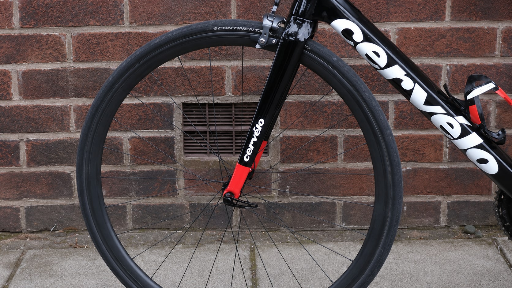 Front wheel of a black and white Cervélo road bike with Continental tyre, non-drive side, against a red brick wall.