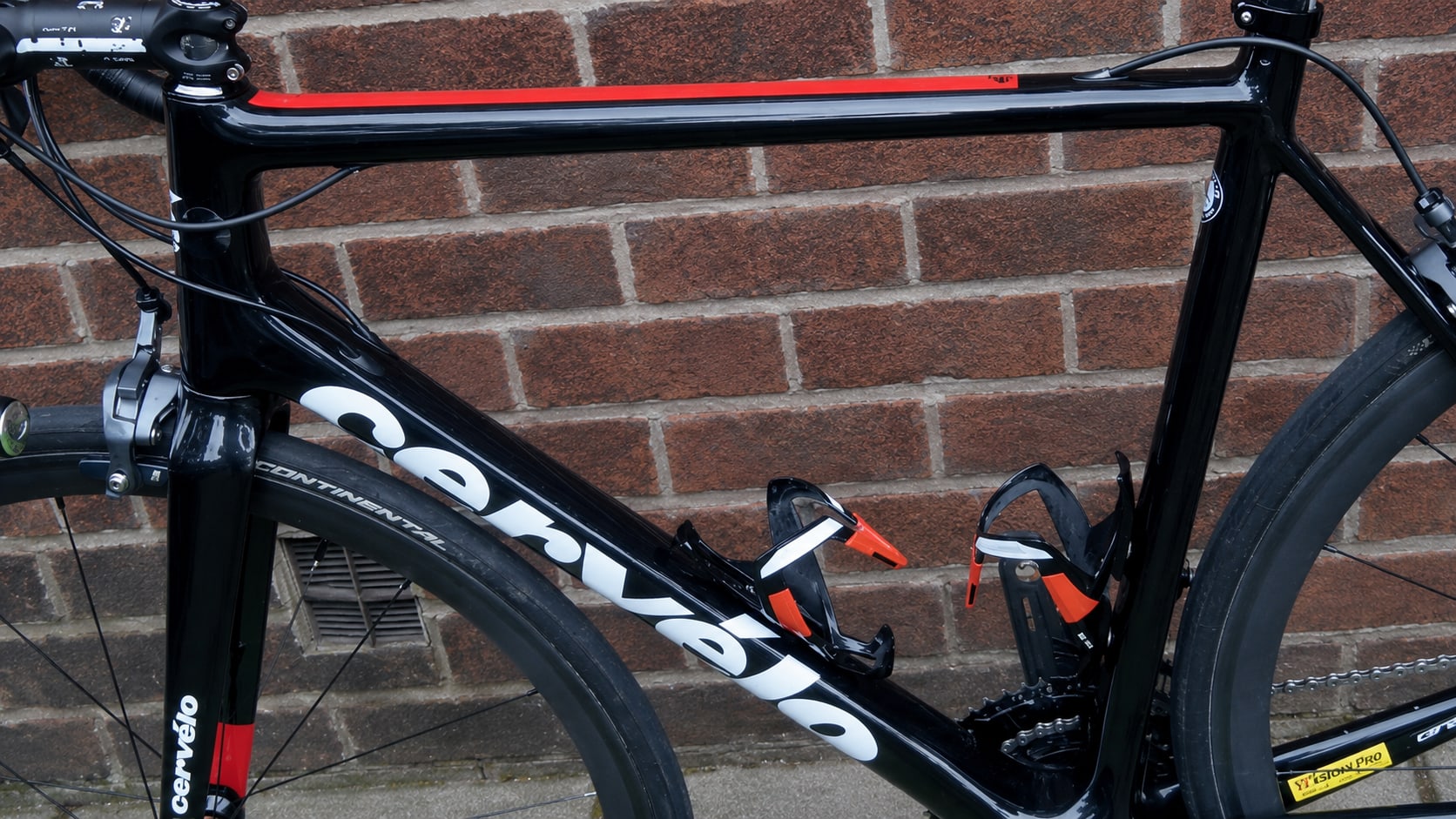 Black and red Cervelo road bike against a brick wall, drive side, handlebars and saddle visible with drop bars and red brake levers.