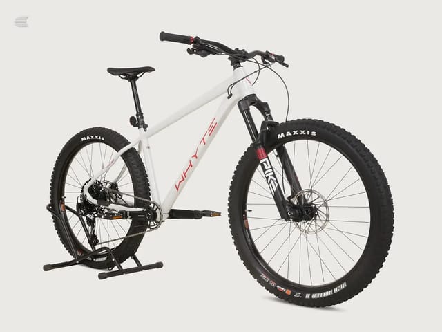 White and red hardtail mountain bike with black Maxxis tyres, displayed on a stand against a neutral background, three-quarter view showing drive side.