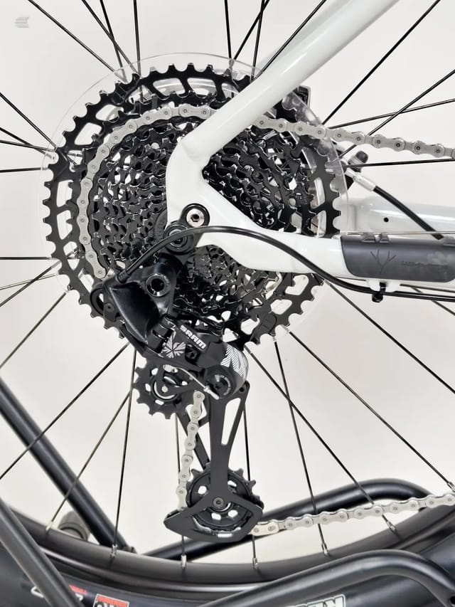 Close-up of white and black mountain bike rear drivetrain, drive side, showing cassette, derailleur, and chain against white background.