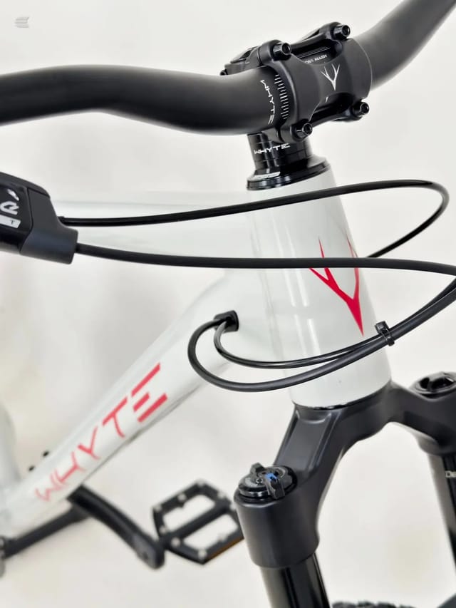Close-up of black stem and handlebars on white and red bike frame, non-drive side, against neutral background.