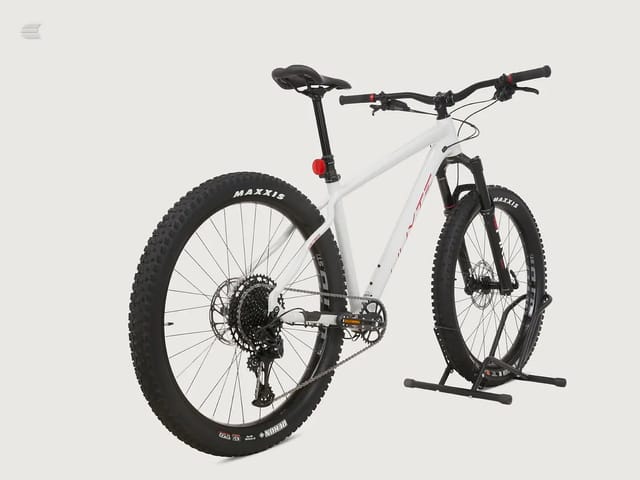 White hardtail mountain bike with red accents on a black stand, drive side view, against a plain grey background.