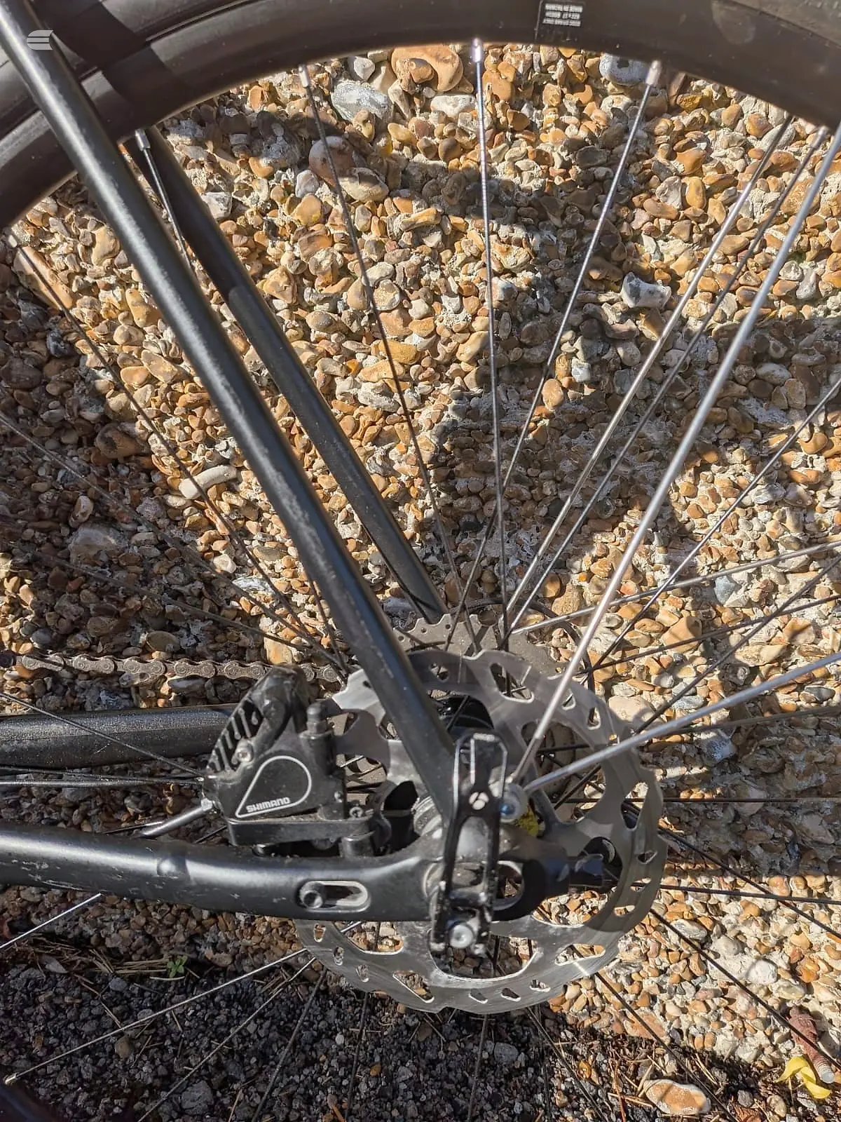 Close-up of front wheel and lower frame of black mountain bike on gravel and stone ground, drive side angle.