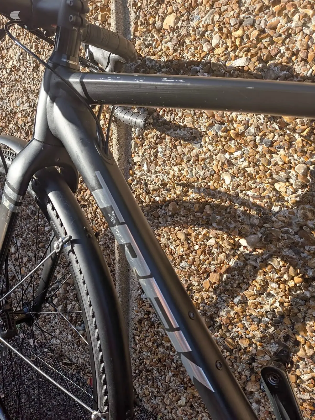 Black gravel or cyclocross bike frame, drive side, on gravel ground with sunlight casting shadows on the tubes and seat tube detail.