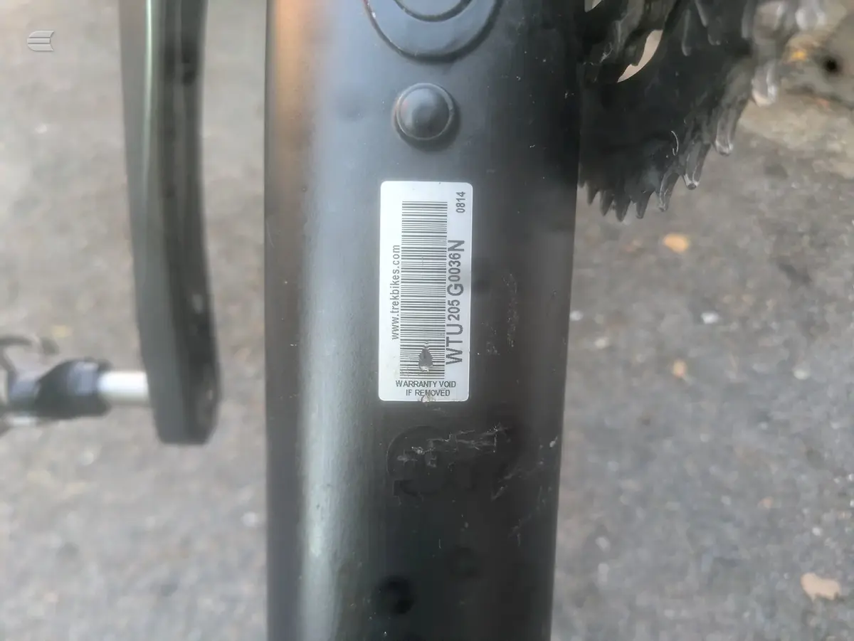 Close-up of black bicycle seatpost with barcode label and warranty void sticker, ground-level angle.