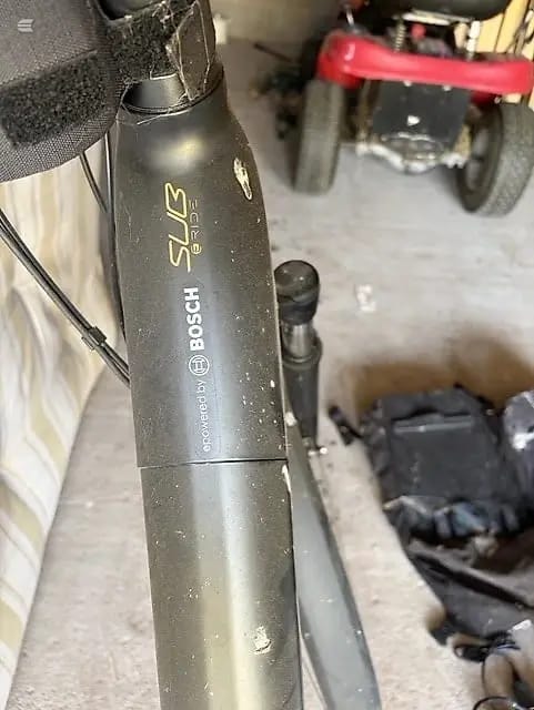 Close-up of Bosch Kiox display unit on black e-bike frame, head tube area, indoor garage setting with red bike visible behind.