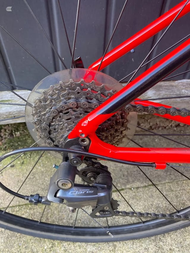 Red road bike rear cassette and derailleur, close-up of drivetrain with Shimano Claris component visible, drive side.