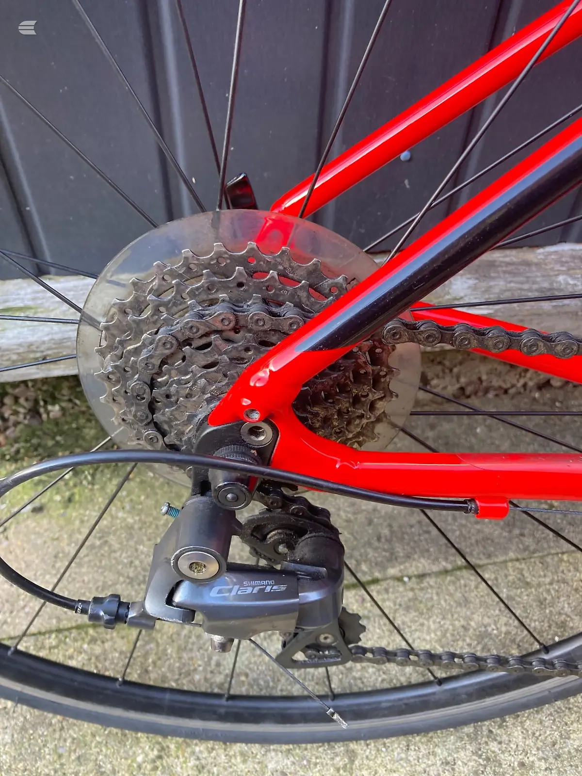 Red road bike rear cassette and derailleur, close-up of drivetrain with Shimano Claris component visible, drive side.