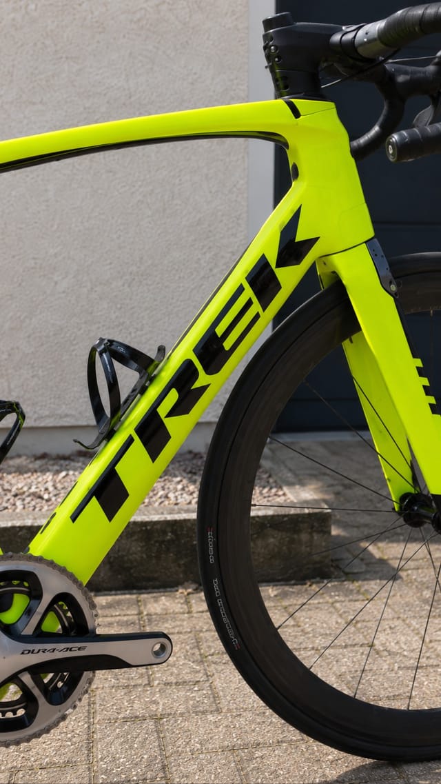 Neon yellow road bike frame, drive side, leaning against concrete wall. Close-up of seat tube and down tube with black geometric branding.